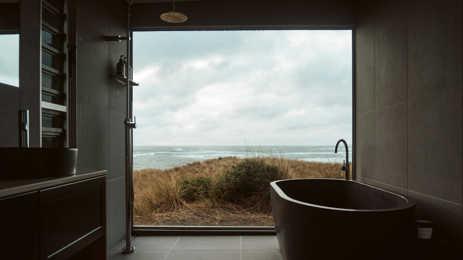 Sunlit coastal bathroom with a freestanding tub beside a large window